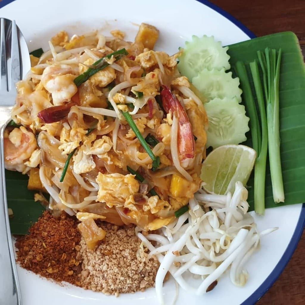 A plate of pad Thai with prawns, bean sprouts, lime and cucumber.