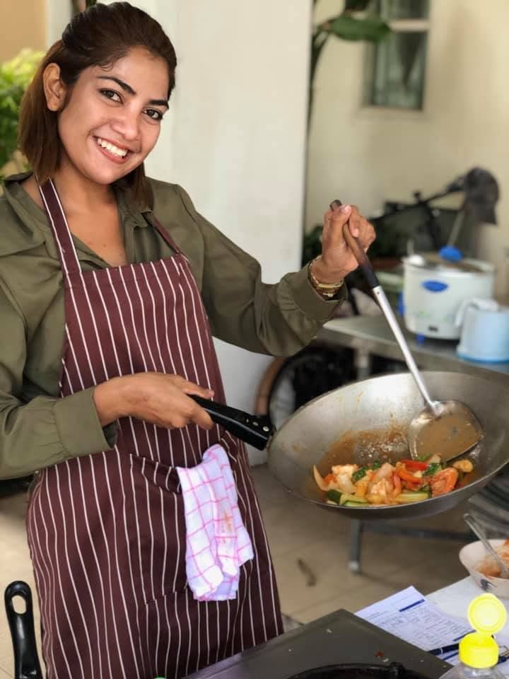 A cook holding a wok of stir-fried vegetables and prawns.